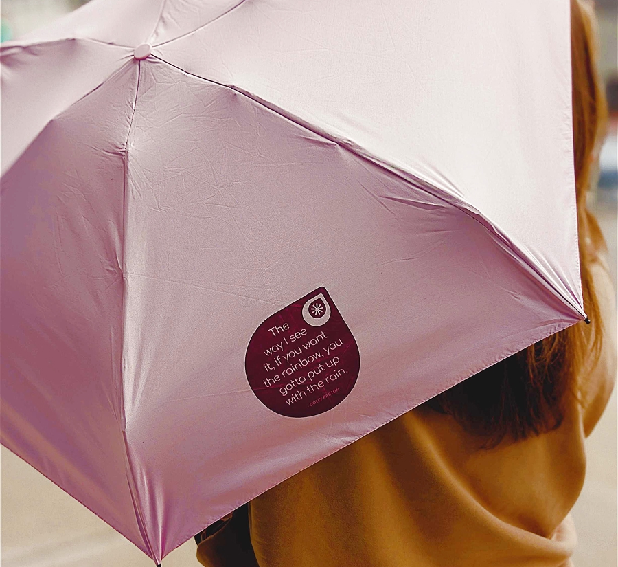 Woman holding pink umbrella with a Dolly Parton quote printed on it