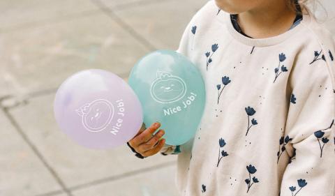 Child holding balloons with cartoon sloth design on them.